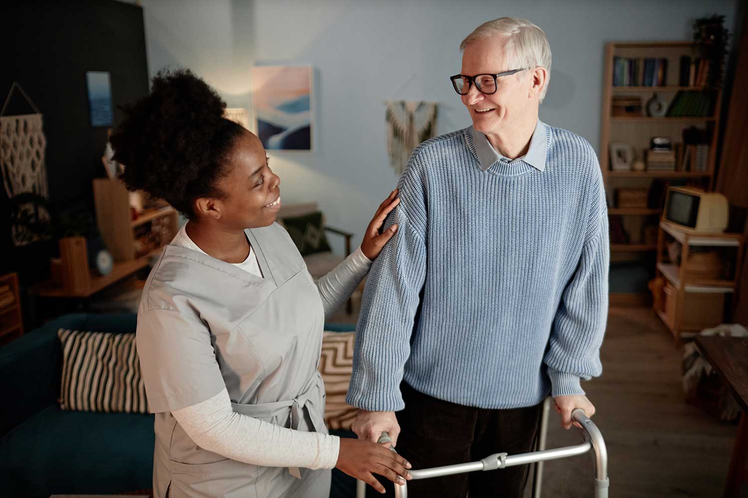 Smiling personal aide helping a senior man safely use a walker at home, showing hands-on senior care, fall safety support, and respectful daily assistance in Pasco County and Pinellas County, Florida