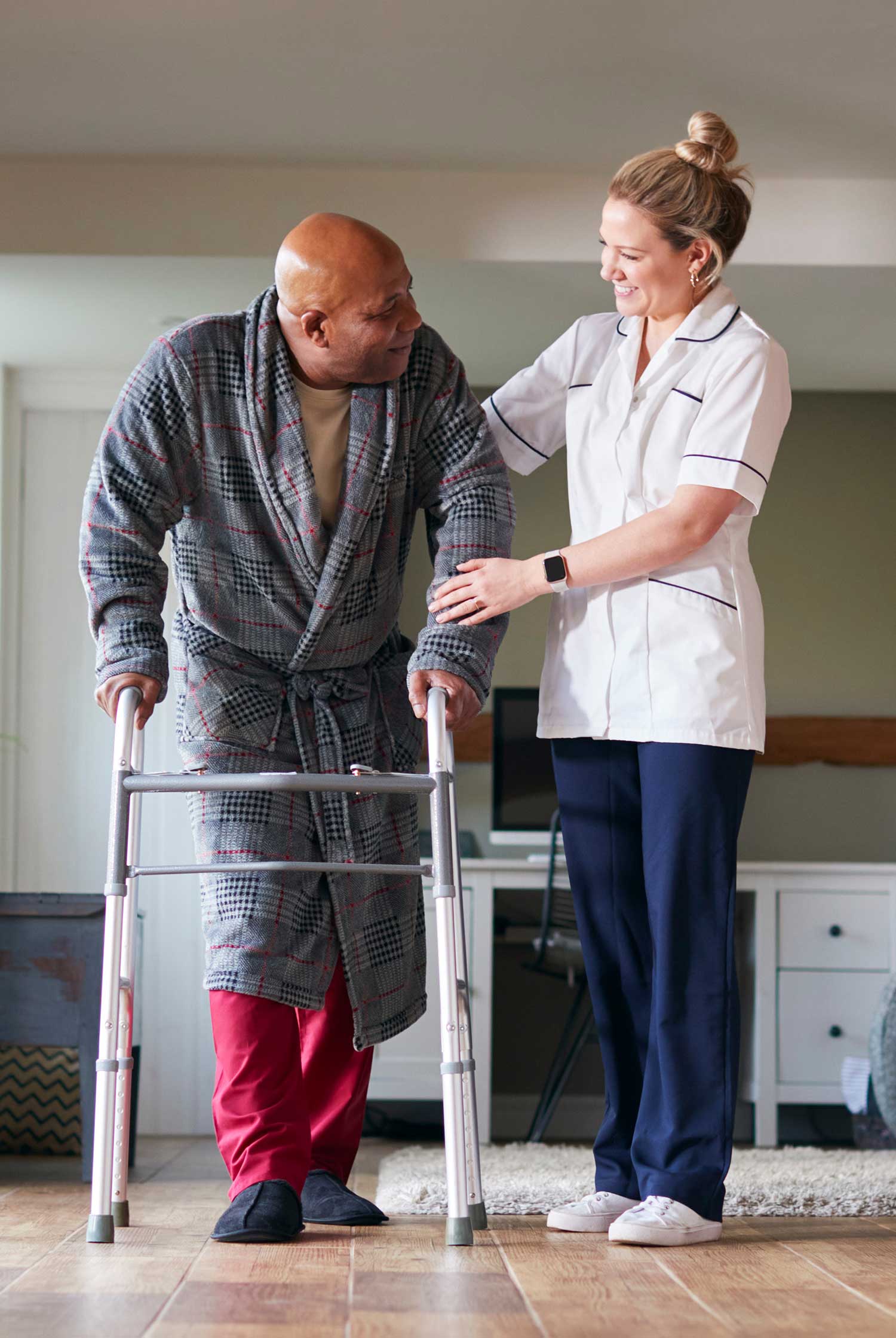 Personal aide helping a senior man safely walk with a walker in his home, showing hands-on senior mobility assistance and fall safety support for families in Pasco County and Pinellas County, Florida